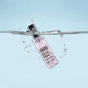Bottle of cosmetic product in water with splashes on color backg