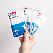 Hand holding multiple 'The Edge' product packets on a white background