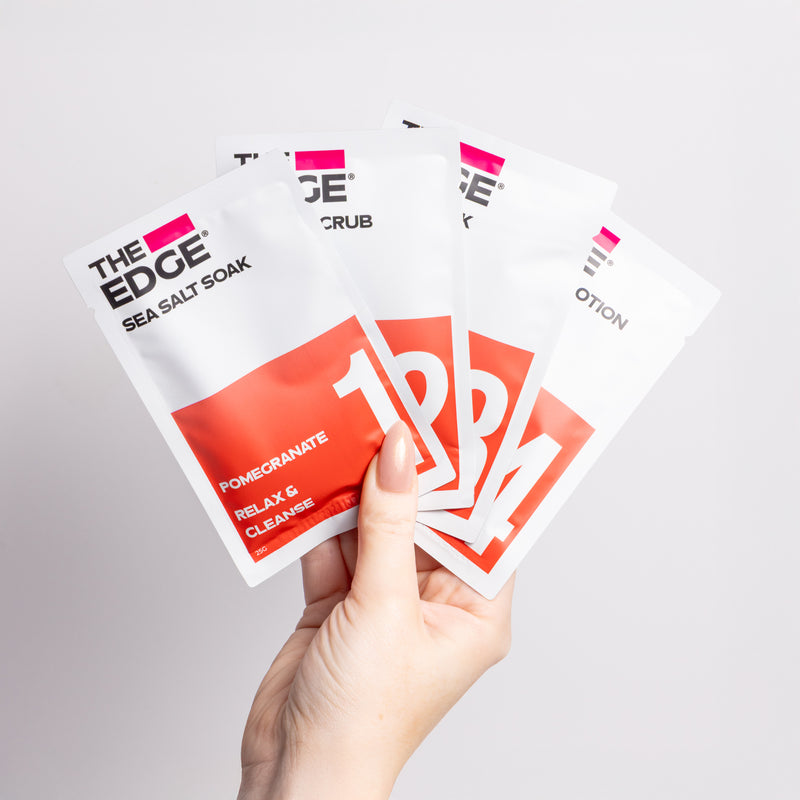 Hand holding multiple 'The Edge' product packages on a light gray background
