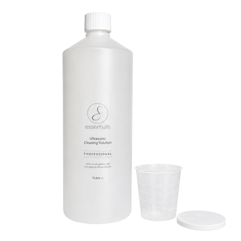 A 1 litre white bottle of 'essentials' Ultrasonic Cleaning Solution with its clear plastic measuring cup and white lid placed beside it on a seamless white background.